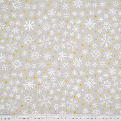 falling snowflakes and gold stars are printed on a silver polycotton fabric with a cm ruler at the bottom