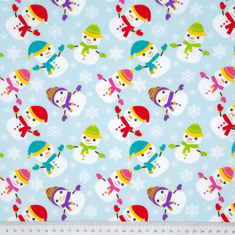 Happy scattered snowmen and snowflakes are printed on a light blue polycotton fabric with a cm ruler at the bottom