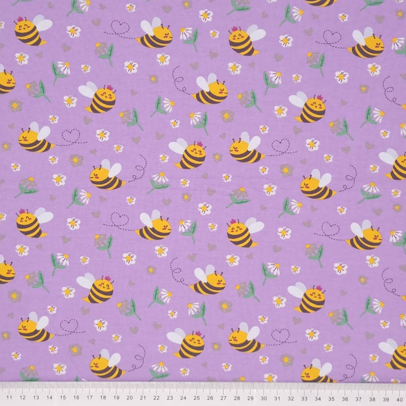 Smiling bees, flowers and hearts printed on a lilac cotton jersey fabric with a cm ruler at the bottom