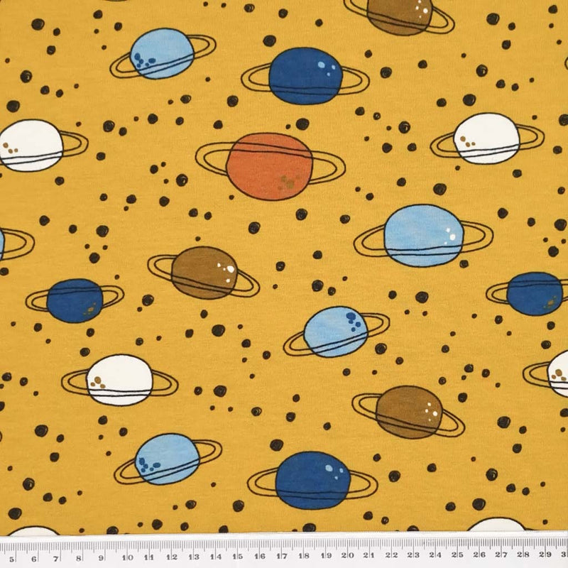 An on trend mustard coloured, 4 way stretch, single cotton jersey fabric featuring planets and rings with a cm ruler