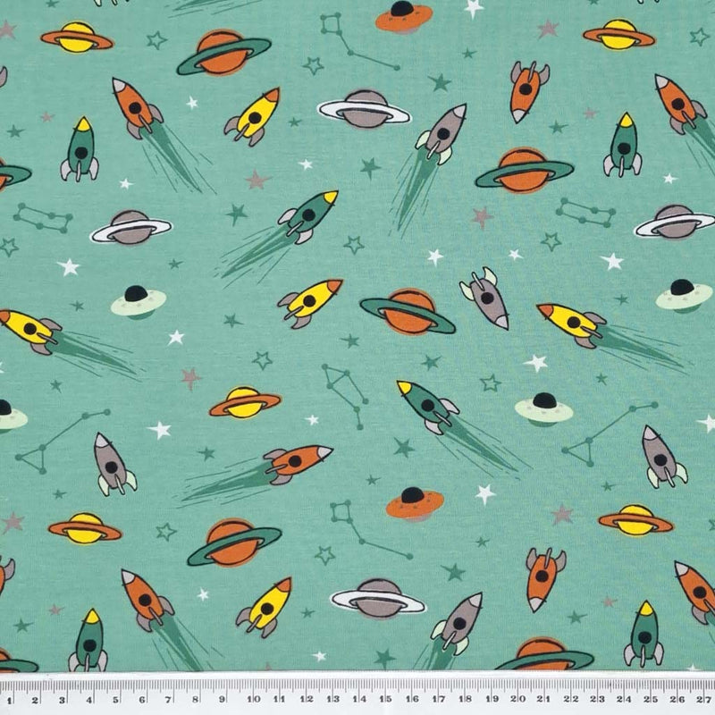 Flying space rockets printed on a green cotton jersey fabric with a cm ruler