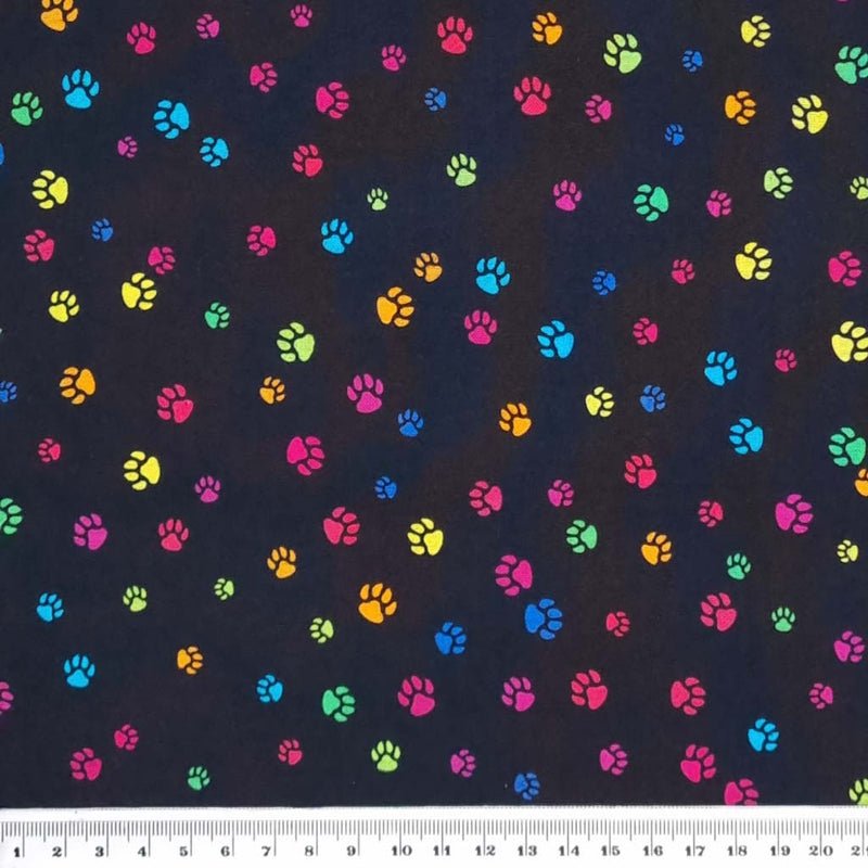 Bright, colourful dog paw prints printed on a black, quality 100% cotton fabric with a cm ruler