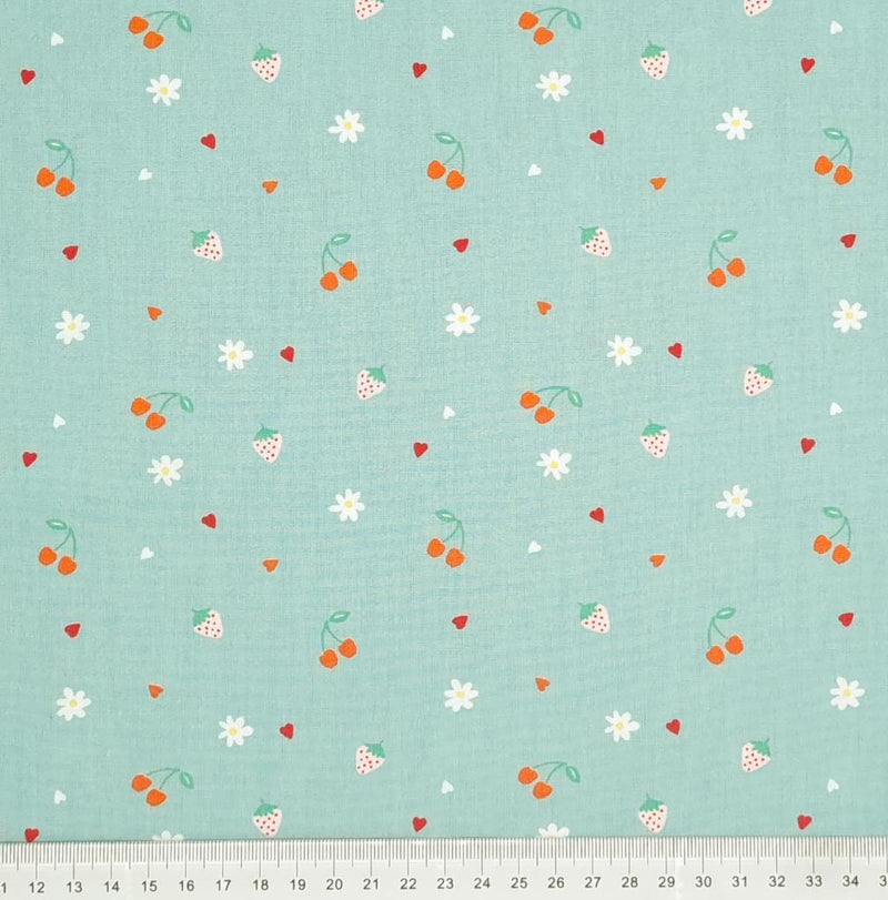 Cherries, strawberries, flowers and hearts are printed on a mint coloured cotton poplin with a cm ruler at the bottom