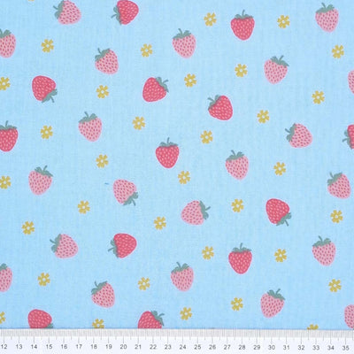 Red and pink strawberries with little yellow flowers are printed on a light blue double gauze fabric with a cm ruler at the bottom