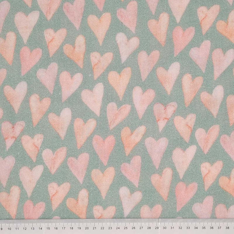 Large rose coloured hearts printed on an organic, mint double gauze fabric with a cm ruler at the bottom