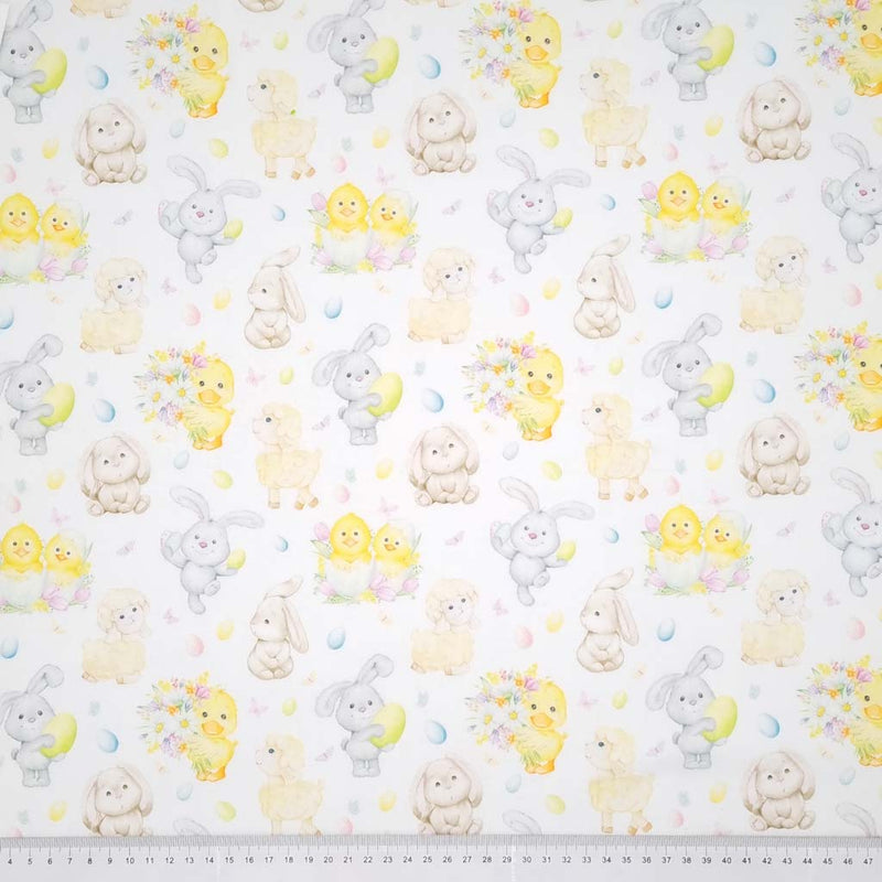 Easter bunnies, spring lambs , chicks and ducks are printed on a white cotton fabric with a cm ruler at the bottom