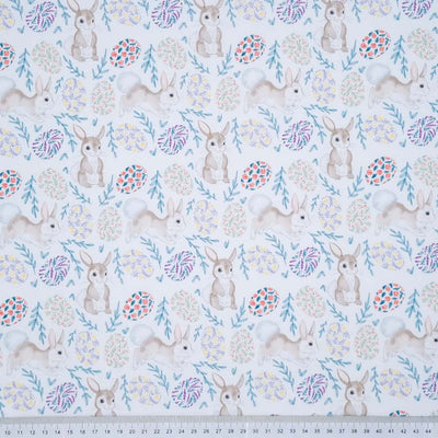 Easter bunnies and eggs in muted tones are printed on a white 100% cotton fabric with a cm ruler at the bottom