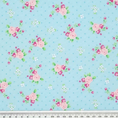 A beautiful pink, vintage blooming rose polycotton fabric print on a turquoise blue background with a cm ruler