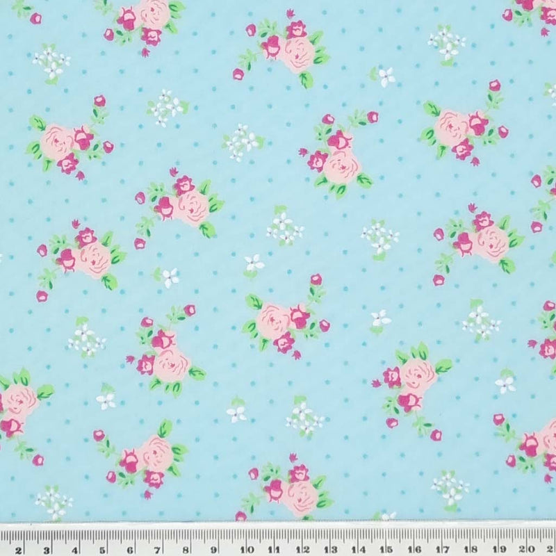 A beautiful pink, vintage blooming rose polycotton fabric print on a turquoise blue background with a cm ruler