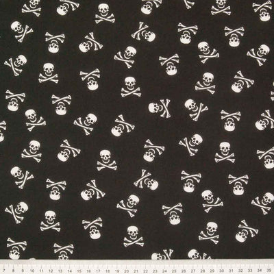 Small white skull and crossbones are printed on a black halloween polycotton fabric with a cm ruler at the bottom