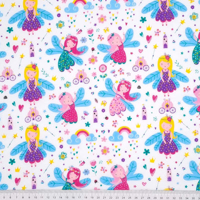 Flying and dancing fairies with colourful rainbows, flowers and carriages are printed on a white polycotton fabric with a cm ruler at the bottom