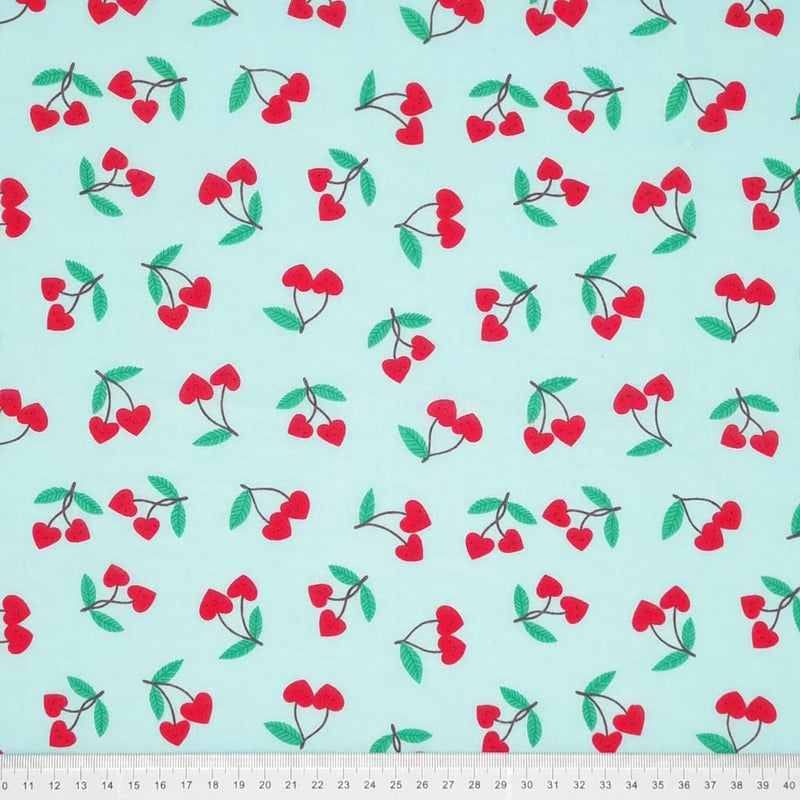 Smiling red heart shaped cherries printed on a sky blue polycotton fabric with a cm ruler at the bottom
