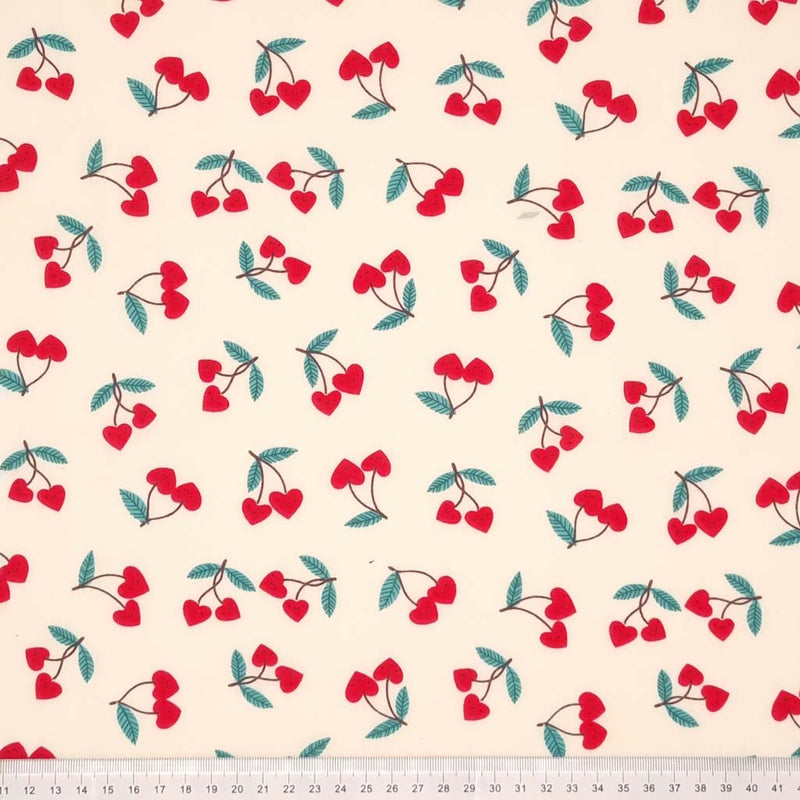 Red heart shaped cherries printed on a cream polycotton fabric with a cm ruler at the bottom