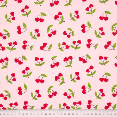 Red heart shaped cherries printed on a pale pink polycotton fabric with a cm ruler at the bottom
