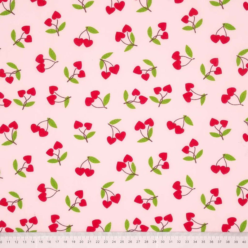 Red heart shaped cherries printed on a pale pink polycotton fabric with a cm ruler at the bottom