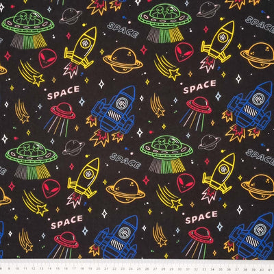 Multi-coloured planets, space rockets, aliens and stars printed on a black polycotton fabric with a cm ruler at the bottom