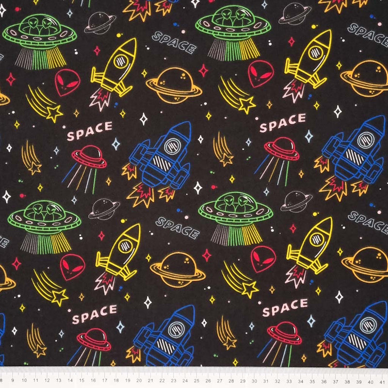 Multi-coloured planets, space rockets, aliens and stars printed on a black polycotton fabric with a cm ruler at the bottom
