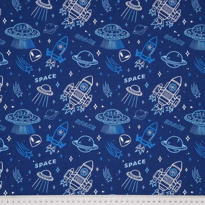 White and blue planets, space rockets, aliens and stars printed on a blue polycotton fabric with a cm ruler at the bottom