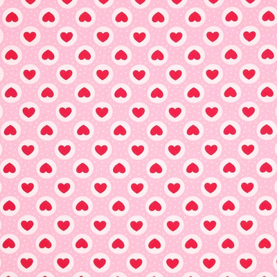 Red hearts and small white spots are printed on a pink cotton poplin fabric by Rose & Hubble