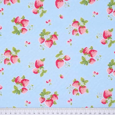 Red strawberries are printed on a sky blue polycotton fabric with a cm ruler at the bottom