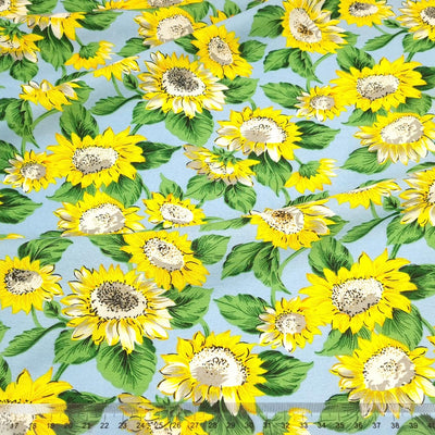 A vibrant sunflower print on a blue rayon mix fabric with a cm ruler at the bottom