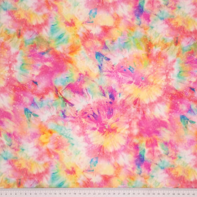 A viscose fabric printed with a colourful tie dye design with a cm ruler at the bottom