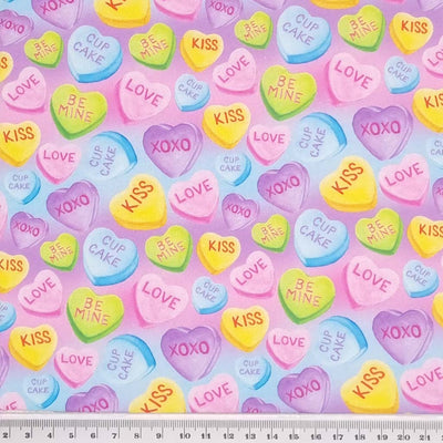 Colourful love heart sweeties printed on a lilac and sky blue cotton fabric with a cm ruler